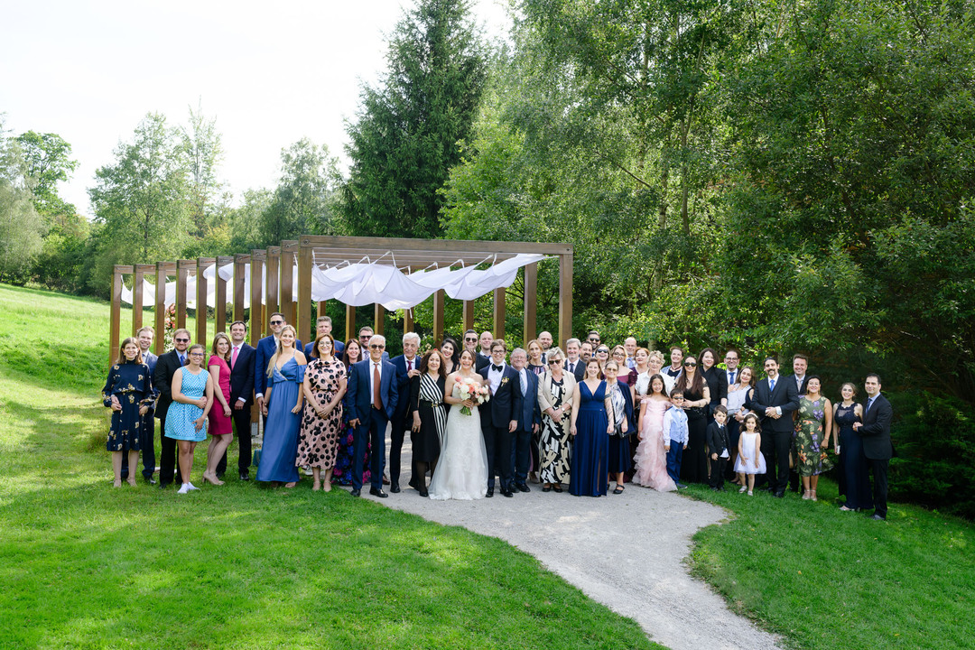 Group photograph of all wedding guests during an outdoor ceremony at Hotel & Garden U Holubů, photographed by Jindřich Nejedlý.
