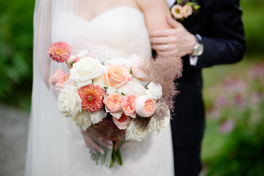 Close-up of the bride holding a pastel wedding bouquet with peonies, roses and dahlias.
