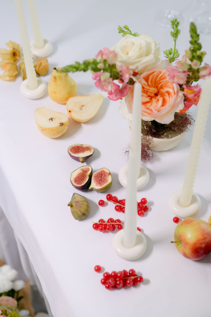 Detail of a set table with flowers, candles and sliced fruit in soft pastel tones during a wedding at U Holubů.
