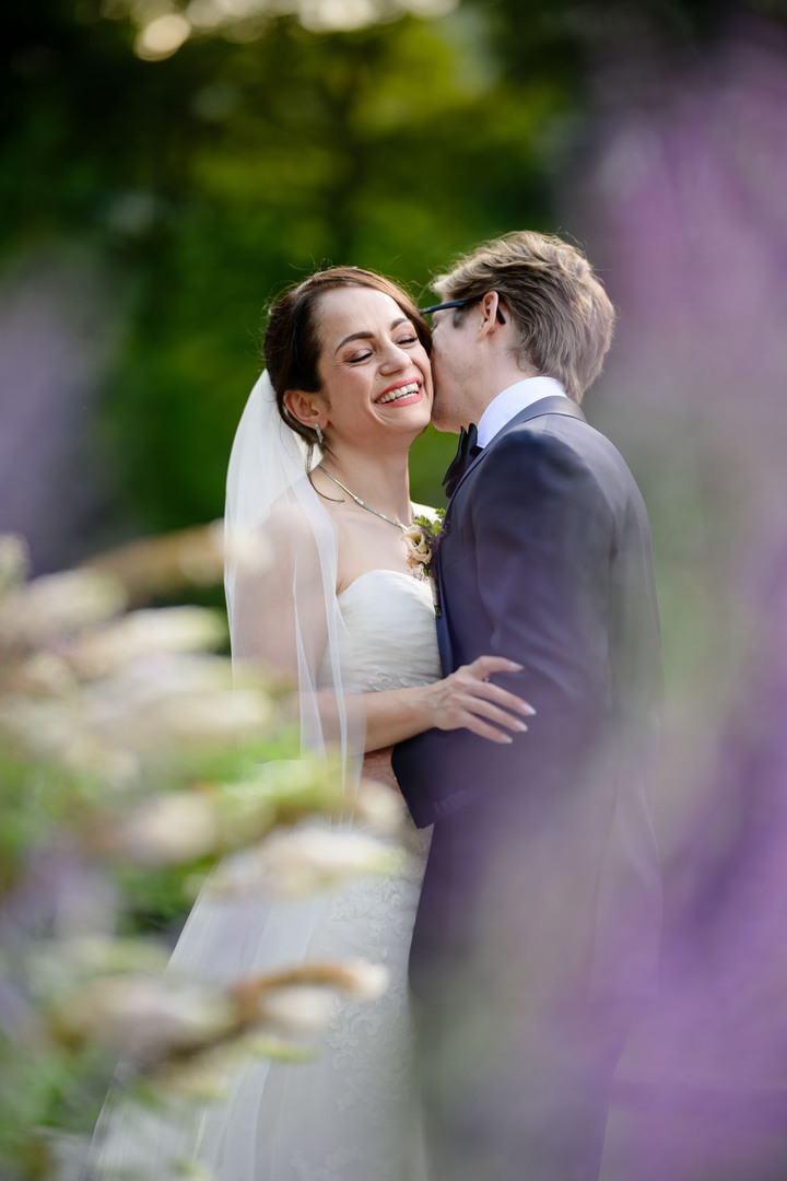 Happy bride and groom sharing a tender kiss in a blooming garden, surrounded by purple flowers, wedding at Hotel U Holubů, Čeladná, Beskydy.
