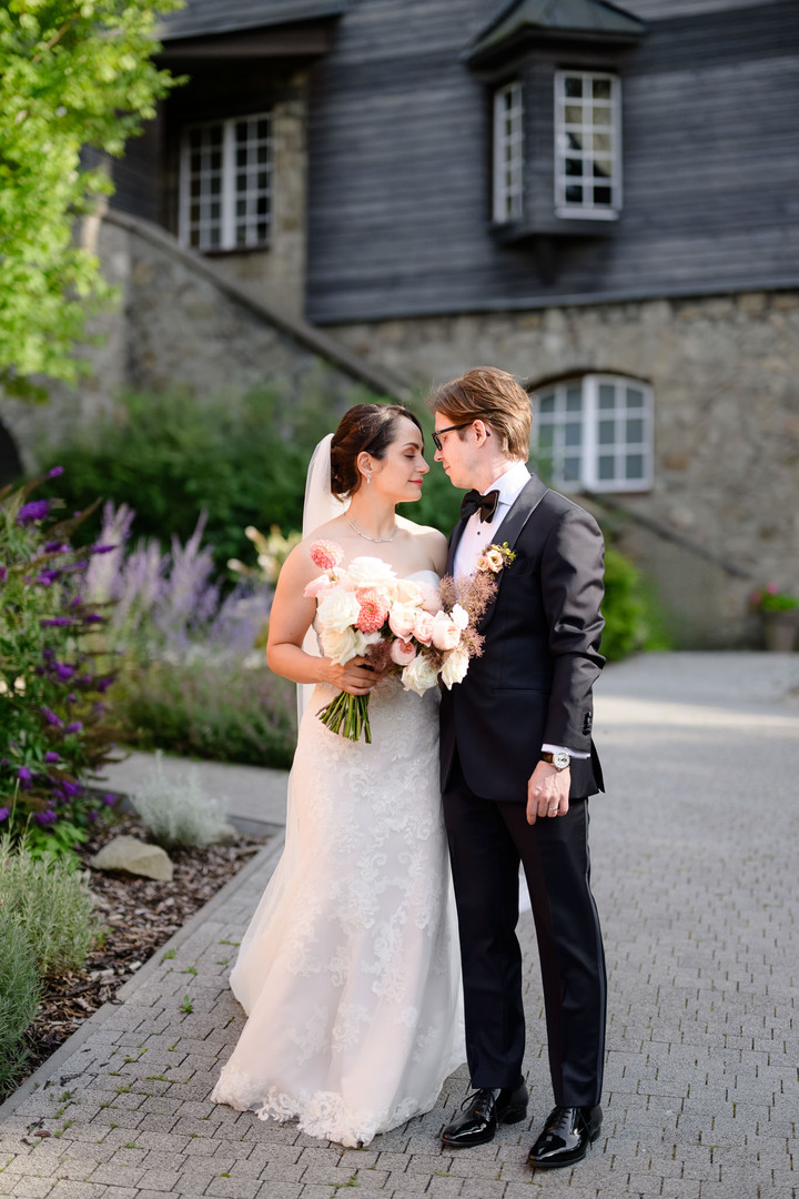 The newlyweds standing close together in front of the stone building of Hotel & Garden U Holubů in the Beskydy.
