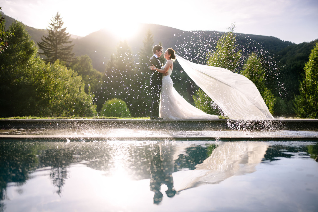 Evening portrait of newlyweds at sunset, embracing with their reflection visible in the water, photographed by Jindřich Nejedlý.