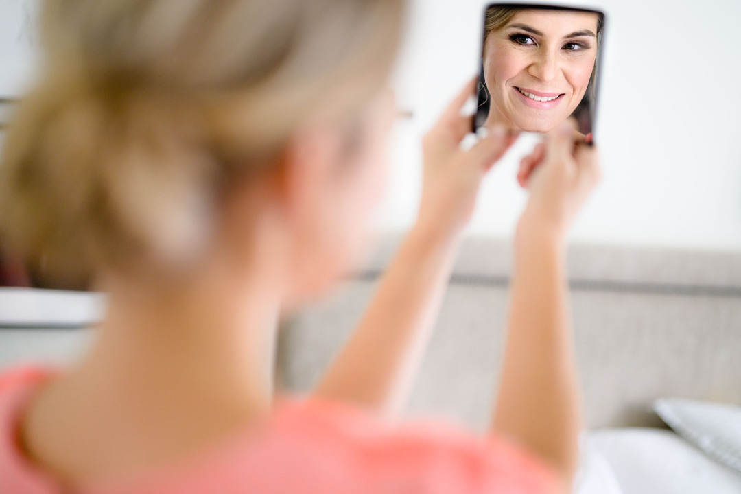 Nevěsta se usmívá sam na sebe do zrcátka během ranních příprav.