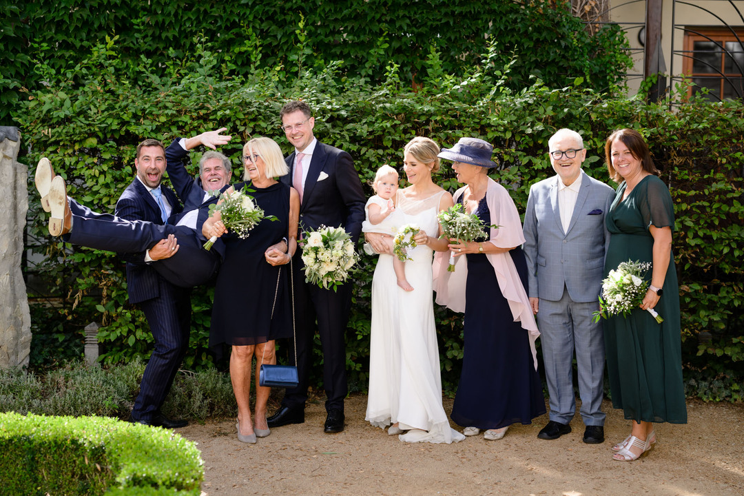 Veselá fotka, kde svědek drží v náručí tatínka, nevěsta drží svou dcerku, ostatní dámy drží kytice. Všichni se vesele smějí.