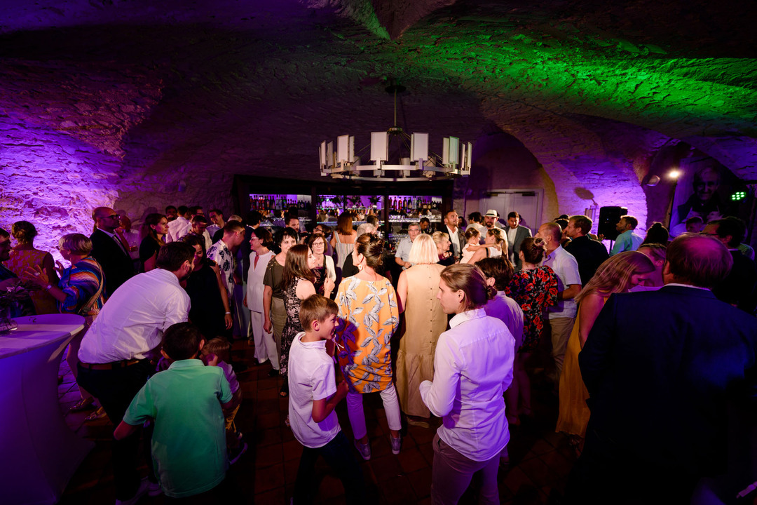 Živá svatební párty plná hostů ve fialově osvětlené kamenné místnosti hotelu Augustine.