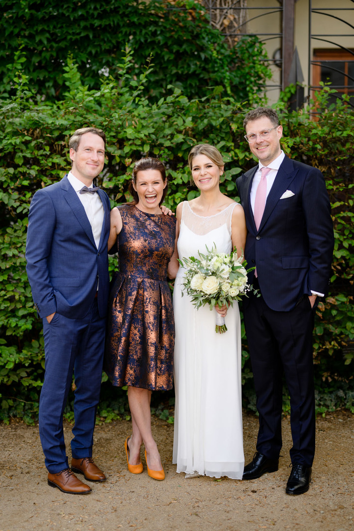 Novomanželé pózují se svými kamarády - mužem v modrém obleku s modrým motýlkem a ženou v modrozlatých šatech a hořčičných lodičkách.