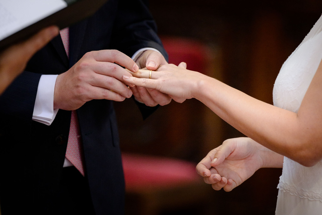 Blízký záběr na to, jak ženich drží nevěstinu ruku a nasazuje ji prsten.
