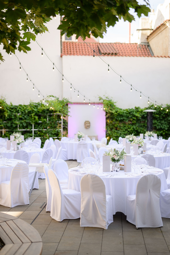 Elegantní venkovní recepce připravená na zahradě hotelu Augustine, celá v bílém provedení s jemnou květinovou výzdobou.