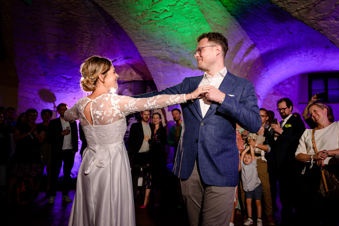 Nevěsta a ženich radostně tancují pod barevnými světly, obklopeni hosty v Pivnici U sv. Tomáše v hotelu Augustine.
