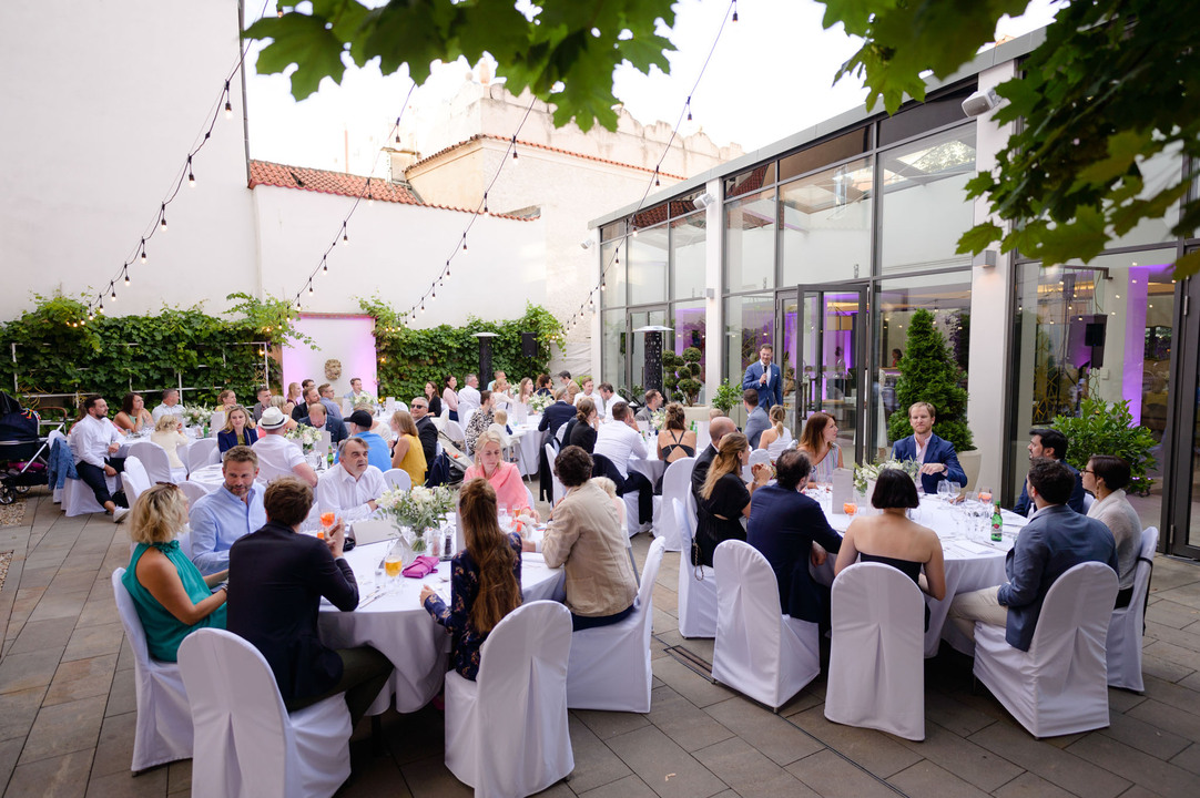 Venkovní recepce, hosté sedí u stolu a ženich má proslov v hotelu Augustine.