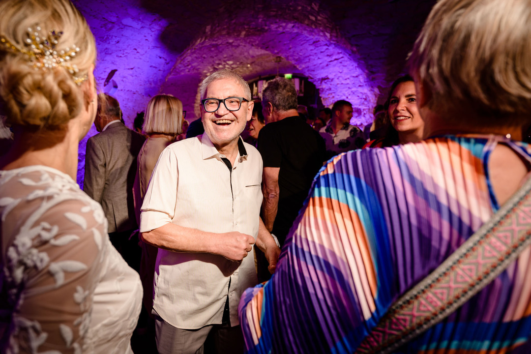 Hosté tancují, baví se a usmívají na svatební hostině v hotelu Augustine, obklopeni fialovým osvětlením.