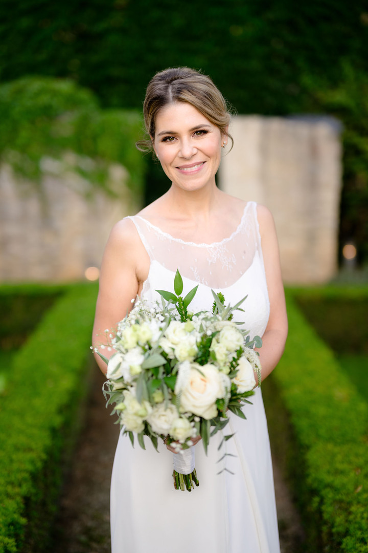 Nevěsta stojí v zahradě Augustine hotelu, a usmívá se do fotoaparátu, v ruce drží svou svatební kytici.
