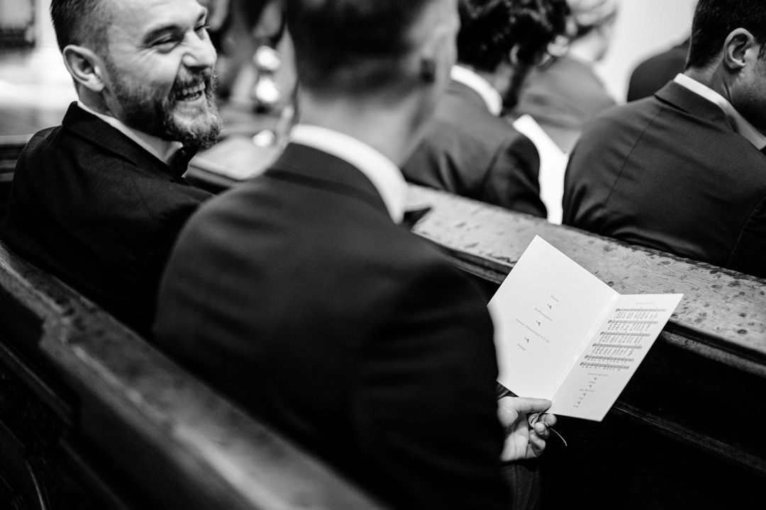 Svatební hosté pozorují obřad v kostele sv. Tomáše a smějí se jeden na druhého.