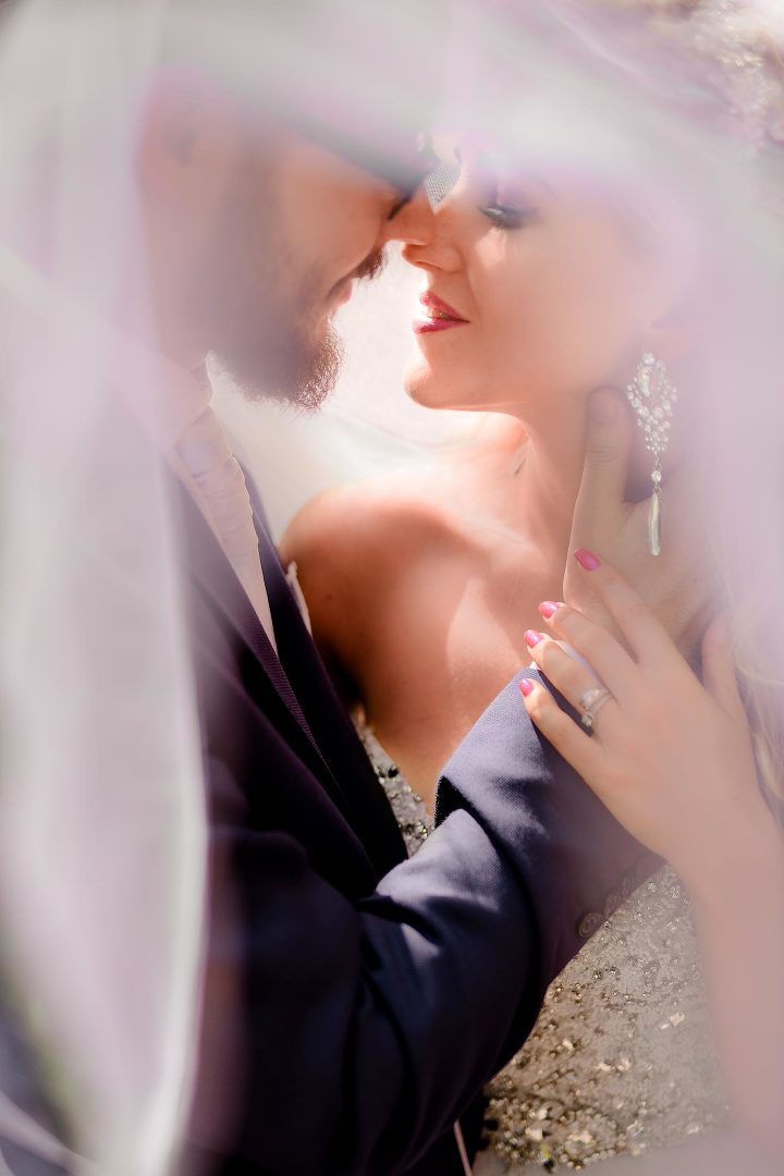 bride with big earing and groom almost kissing under a veil 