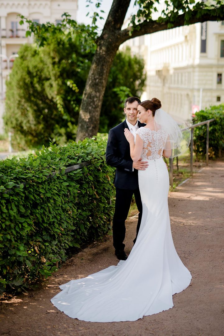 groom in black suit holding bride in white dress in the city park