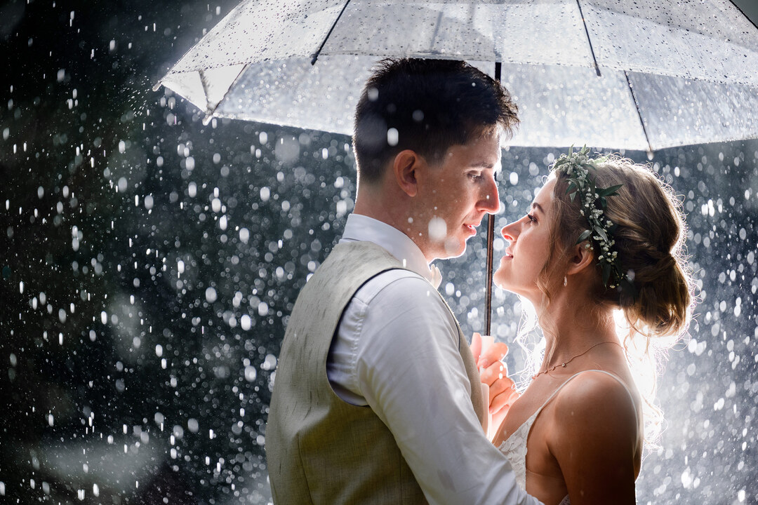 bride and groom under the umbrella during the storm