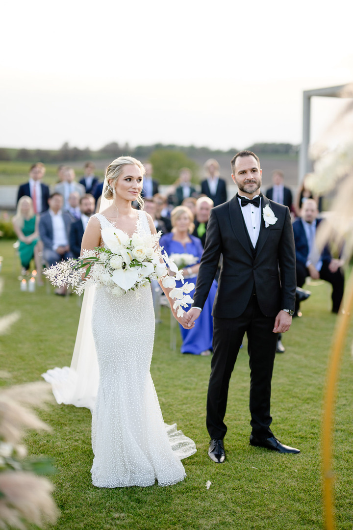 Bride and groom standing hand in hand, surrounded by guests at Obelisk Winery.
