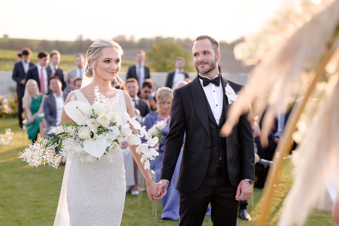 Couple holding hands during their wedding ceremony at Obelisk Winery, with floral decorations.