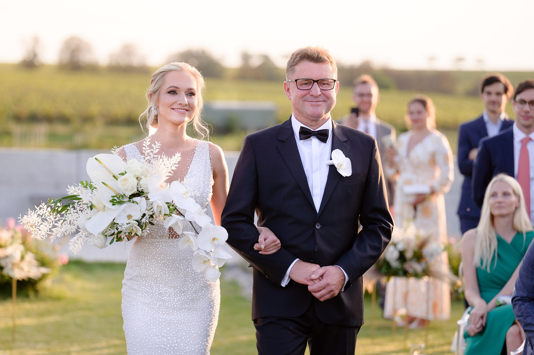 A bride holding a bouquet of flowers, walking with her father at Obelisk Winery.