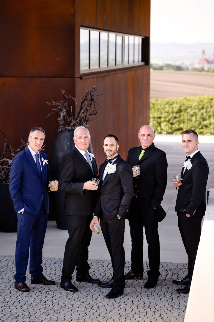 Groom and groomsmen posing with drinks in front of Obelisk Winery.