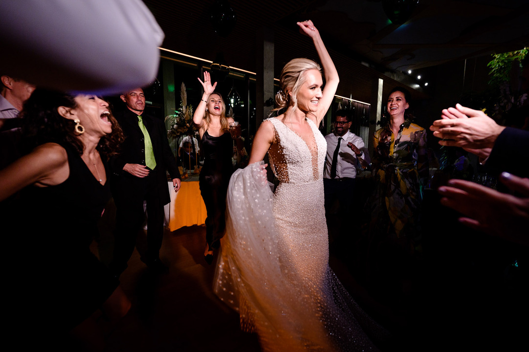 The bride holds her dress and dances, with her hand raised above her head.