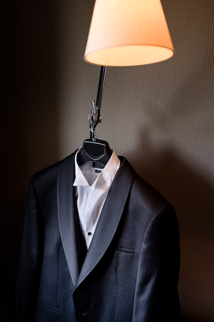 Groom's suit hanging on a lamp, featuring a dark jacket and white shirt.