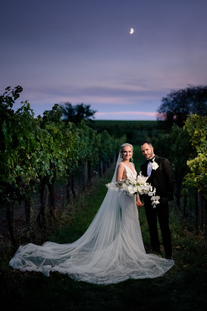 The bride and groom pose at dusk in the vineyard.