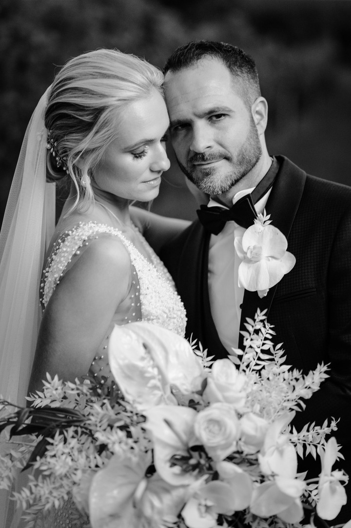 Black and white photo of bride and groom embracing, with the bride holding a bouquet.