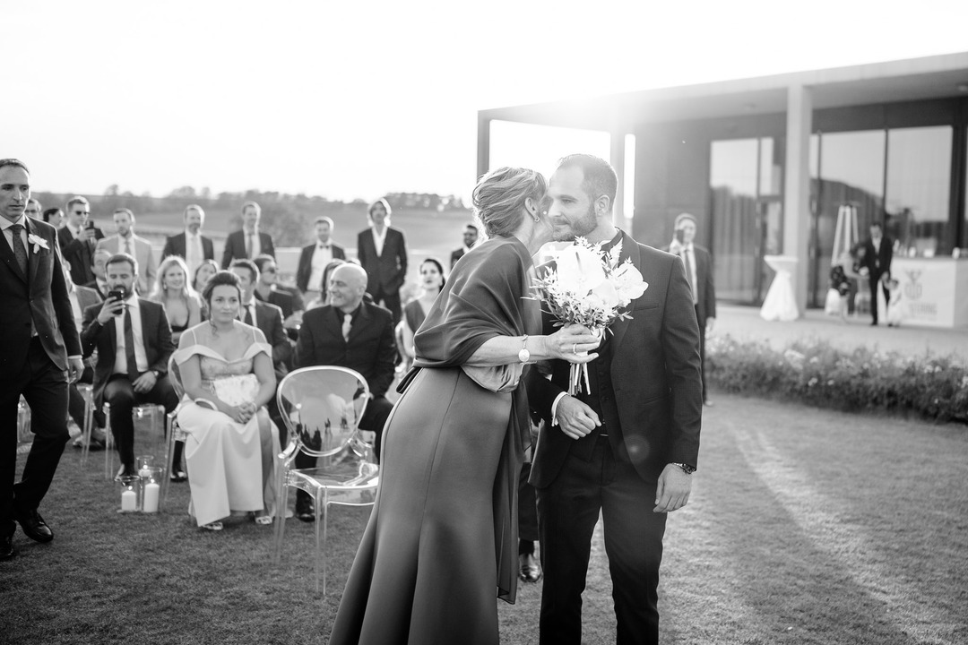 Mother is kissing her son at the ceremony with guests watching at Obelisk Winery.