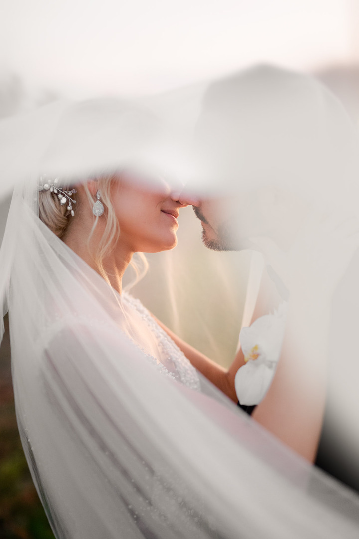 A view of the newlyweds cuddling under the veil, preparing to kiss.