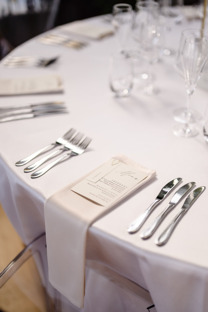 Close-up of a wedding table setting with white tablecloth, silverware, and menu card.