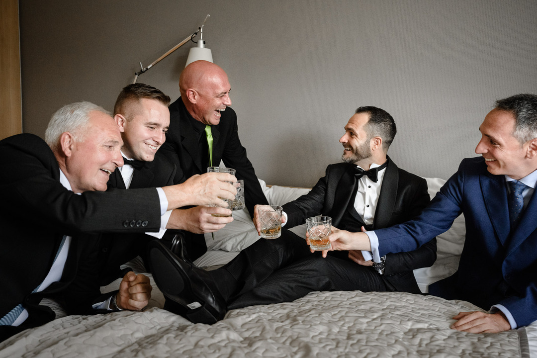 Groom and groomsmen in tuxedos cheerfully toasting with glasses of whiskey at the Obelisk Winery wedding.