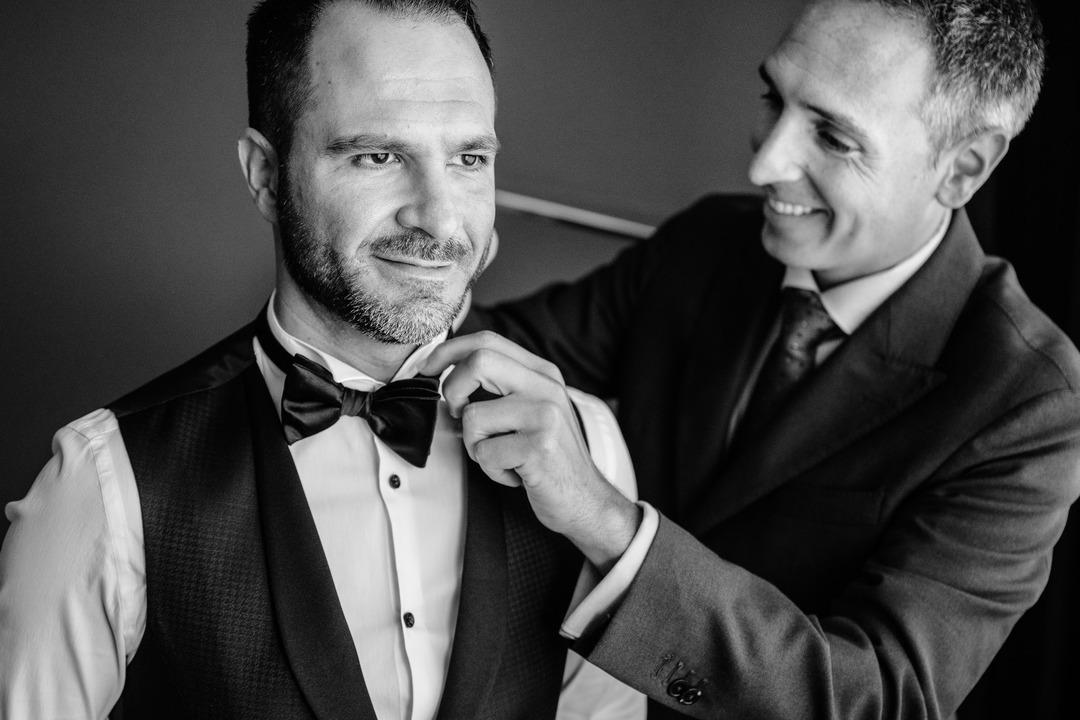 Groom getting help with his bow tie from his brother, he is smiling.