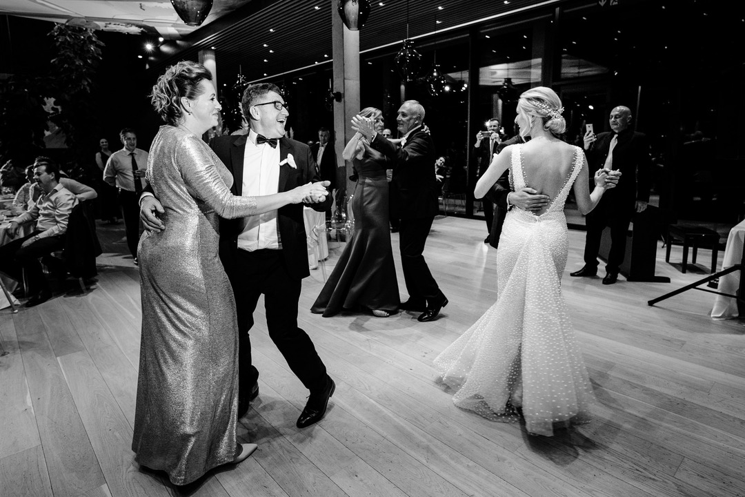 The bride's parents dance while smiling and looking at the dancing newlyweds.