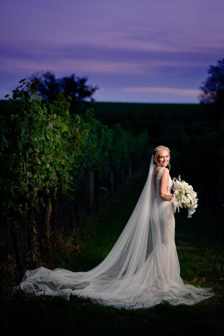 Bride posing elegantly in a vineyard at dusk, holding a bouquet at Obelisk Winery.