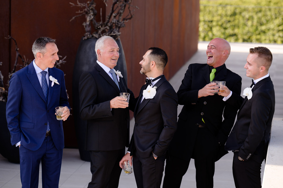 Groom and groomsmen laughing and holding drinks in front of Obelisk Winery.