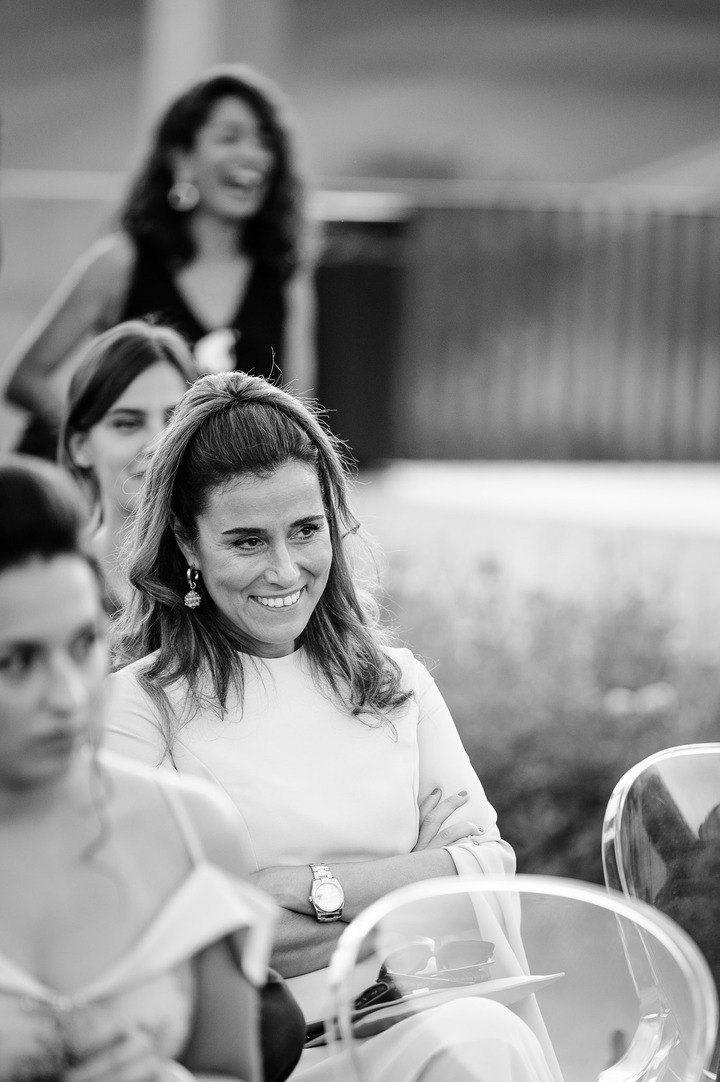 A woman in elegant light dress smiles cheerfully from her chair.