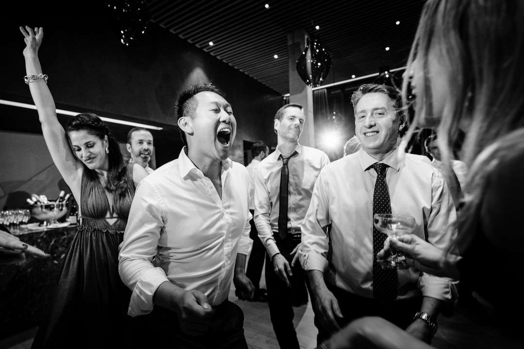 A joyful group of people laughing and celebrating at a wedding reception.
