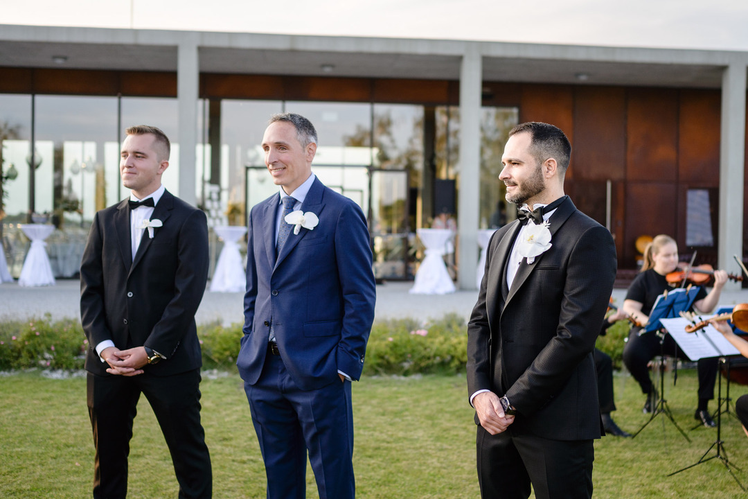 The groom watches the arriving bride, standing next to his best man.