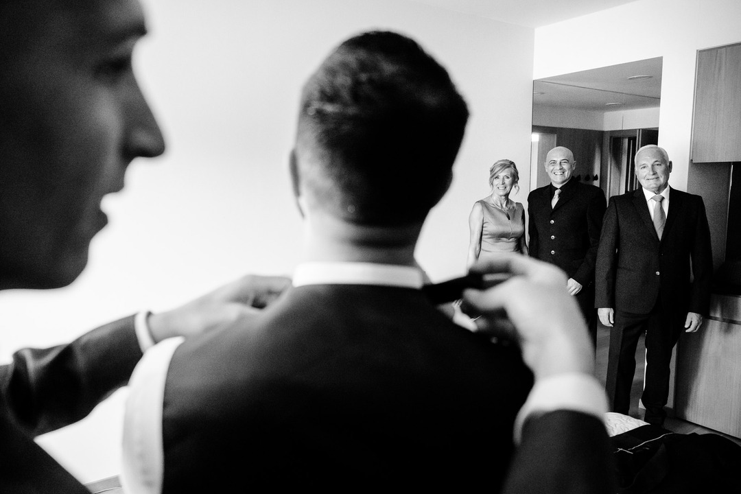 Groom adjusting his bow tie while family members look on at Obelisk Winery.