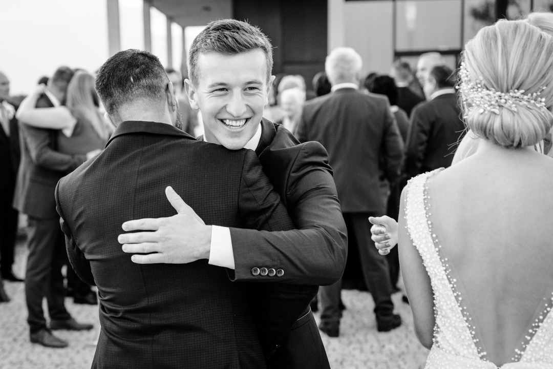 A heartwarming moment at a wedding reception where a man in a suit is smiling broadly while hugging the groom. 