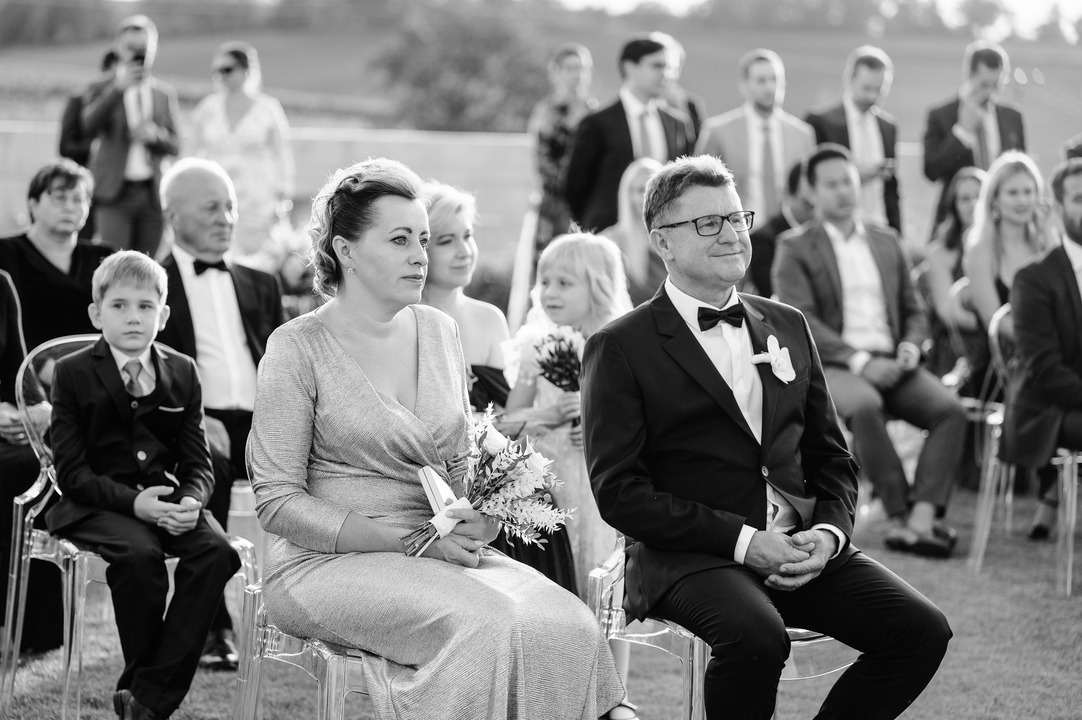 A black and white shot of the bride's parents sitting on a chair, watching the ceremony.