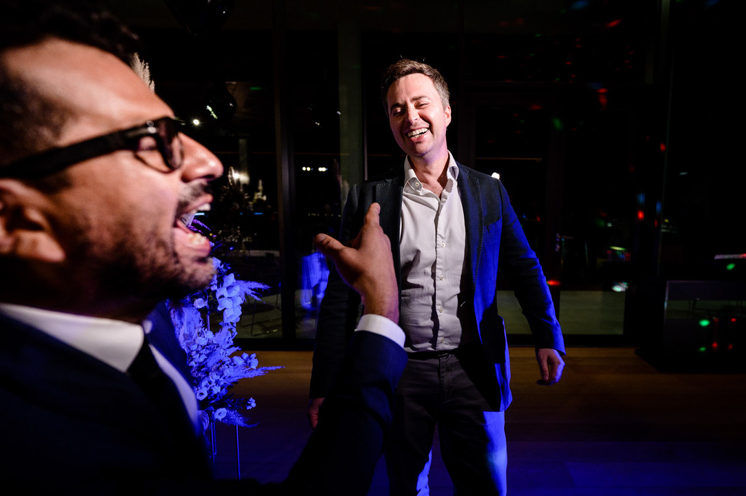 Two men dance together on the dance floor under blue lighting.