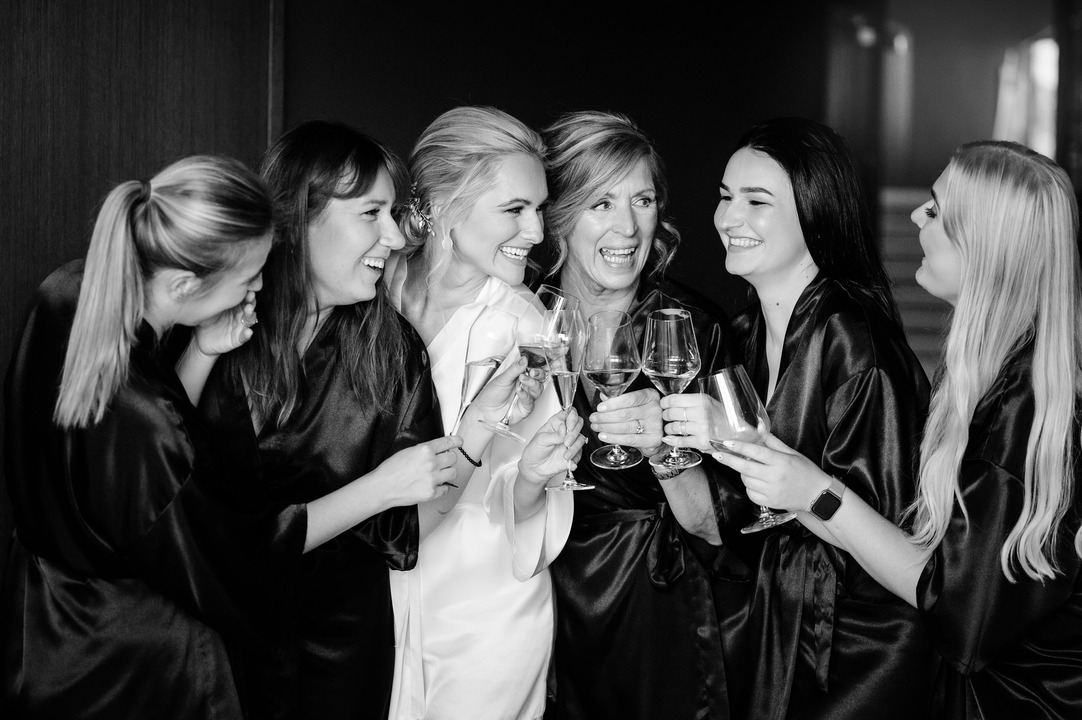 Bride and bridesmaids in robes celebrating with champagne glasses before the wedding.