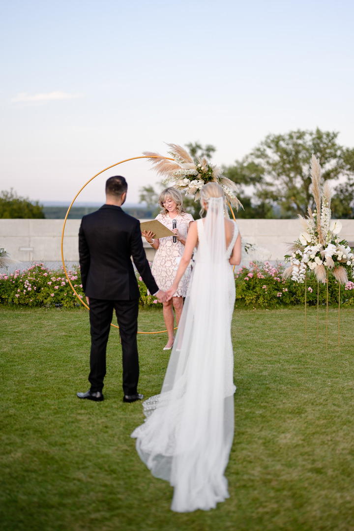 A couple exchanging vows under a floral arch at Obelisk Winery.