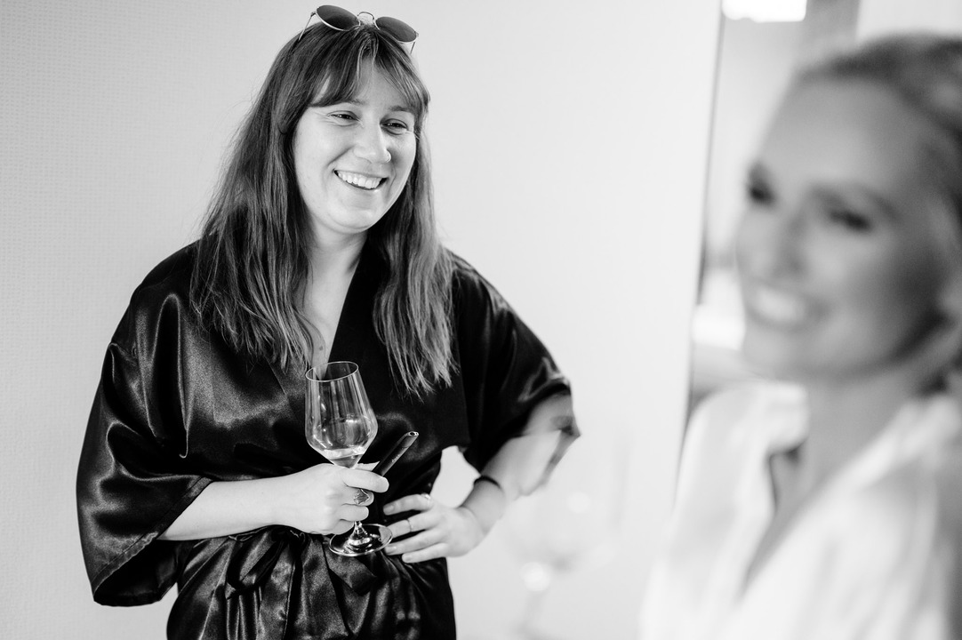 The bride’s bridesmaid enjoys the morning preparations with a smile, holding a glass of wine.