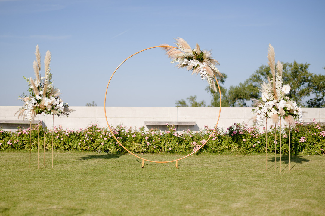  Outdoor wedding ceremony setup with circular arch on a green lawn.