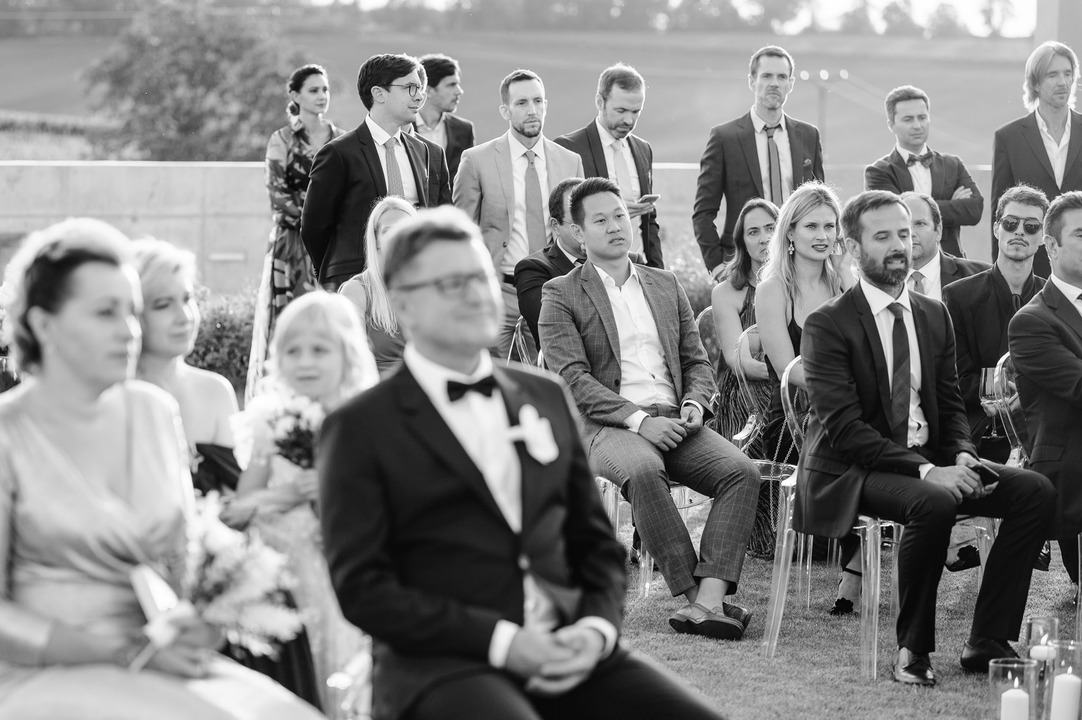 Black and white shot of wedding guests standing during the ceremony.