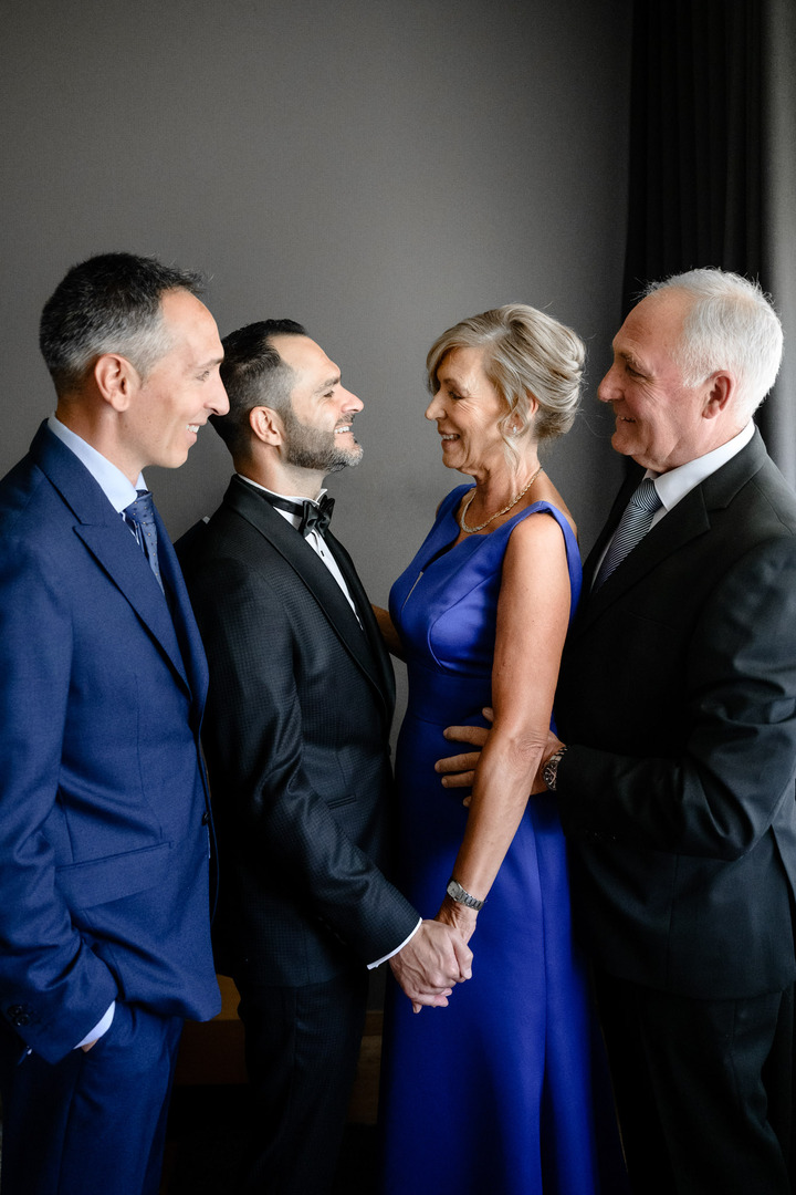 The groom with his mom, dad and brother before the wedding ceremony smiling at each other.