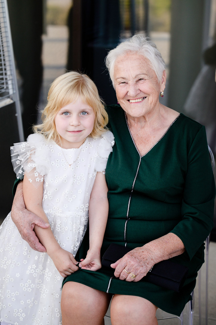 An elderly woman in a green dress sits with a young girl in a white dress at a wedding.